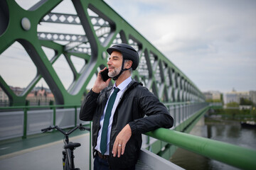 Businessman commuter on the way to work, on bridge, calling on mobile phone, sustainable lifestyle concept.