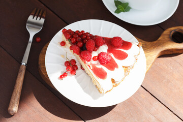 A piece of berry pie with cheese cream on a plate on a wooden background.