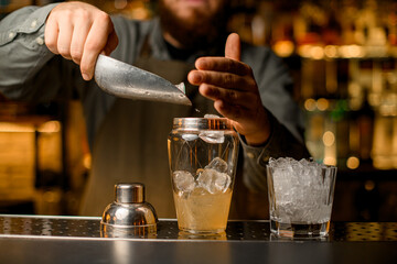 front view of shaker with drink into which bartender pours ice cubes using scoop