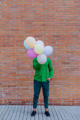 Fun portrait of happy energetic mature man holding balloons in street and hiding behind them, feeling free.