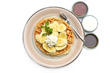 Belgium waffles with sliced banana and ice cream on a plate with chocolate toping and fruit sauce