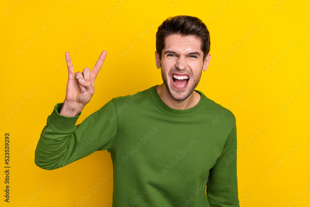 Poster Photo of cool funny guy wear green sweater showing hard rock sign isolated yellow color background