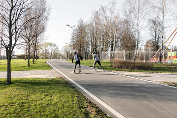 Biathletes in helmets ride roller skis in the park. Adult men ride roller skis. Roller ski training. The concept of competition, biathlon and training. Roller sports.