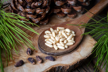 Pine nuts in the spoon and pine nut cone on the wooden table. Organic food.