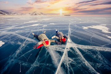 Winter lake Baikal Russia, two tourist women friends in red cap are skating on ice frozen sunset