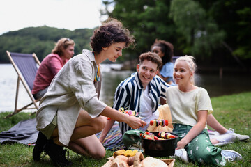 Fototapeta premium Group of multiracial young friends camping near lake and and having barbecue together.