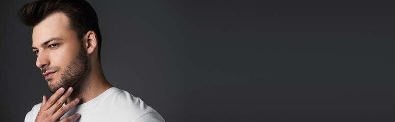 Obraz premium Young man touching beard and looking away isolated on grey, banner.