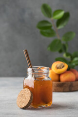 Obraz na płótnie Canvas A jar with apricot jam and a spoon close-up on a gray. Fruit preservation.