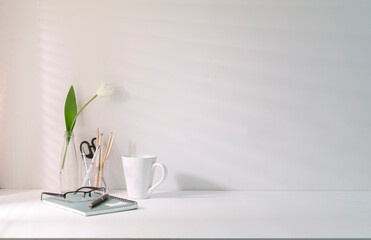 Minimal workplace with coffee cup pencil holder notebook and flower pot on white table. Copy space for your advertise text.
