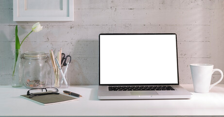 Laptop with blank screen, coffee cup, picture frame and notebook on white table.