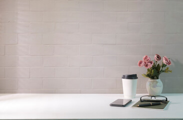 Comfortable workplace with paper cup, flower pot, smart phone and notebook on white table. Copy space for your advertise text.