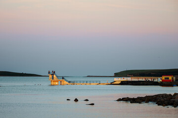 Blackrock diving board with people, Galway city, Ireland. Calm pastel sun rise colors. High tide. Popular town landmark.