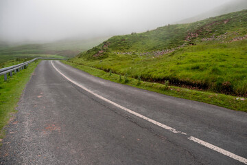 Small narrow asphalt road in a mountains and fog in the background. Dangerous conditions in country side. West of Ireland.