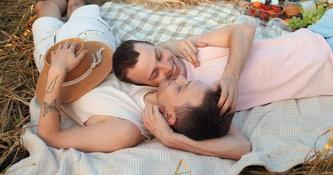 Gay couple having romantic picnic and lying on plaid at the field