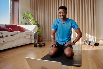 Fototapeta na wymiar Young happy African American black male exercising at home doing an online workout class on a yoga mat in his living room
