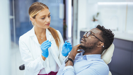 Unhappy african american man in medical chair complains of toothache to female dentist at modern dental clinic. Shot of a young man having a consultation with his dentist