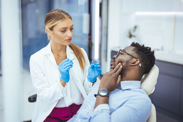 Young black man holding cheek in chair at dentist, having toothache. Young good looking man having...