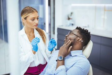 Young good looking man having dental treatment at dentist's office. African guy in dentist chair...