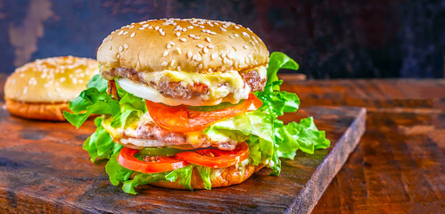 Close-up of delicious fresh homemade burger with lettuce, cheese, onion, and tomato on a rustic wooden plank on a wooden table