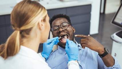 Young black man holding cheek in chair at dentist, having toothache. Young good looking man having dental treatment at dentist's office. Unhappy african american man in medical chair complains