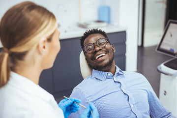 Smiling african guy in dentist chair looking with trust at his doctor, close up. Young African...