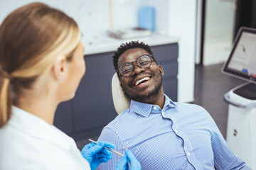Female dentist with happy male patient at clinic. Happy patient sitting on chair while looking at...