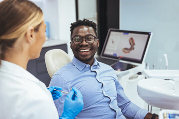 Smiling african guy in dentist chair looking with trust at his doctor, close up. Young African American Man Getting Teeth Treatment With Professional Stomatologist At Modern Clinic, Closeup - Powered by Adobe