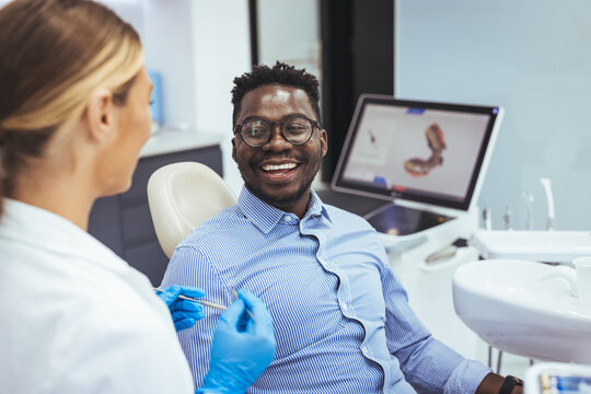 Smiling african guy in dentist chair looking with trust at his doctor, close up. Young African American Man Getting Teeth Treatment With Professional Stomatologist At Modern Clinic, Closeup