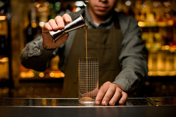 bartender carefully pours drink into transparent glass on the bar counter. Front view