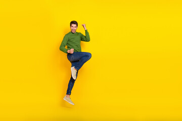 Fototapeta na wymiar Photo of excited lucky guy wear green sweater jumping rising fists empty space isolated yellow color background