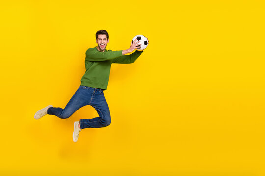 Photo Of Charming Excited Guy Wear Green Sweater Jumping High Catching Ball Empty Space Isolated Yellow Color Background