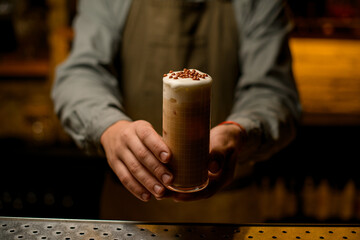 Male hands holds glass of cocktail garnished with whipped cream and chocolate balls