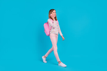 Full length photo of shiny cute little lady dressed dotted pullover rucksack communicating modern device isolated blue color background