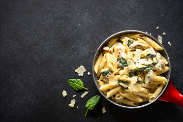 Pasta penne with chicken and spinach in creamy sauceon black table. Top view with copy space.