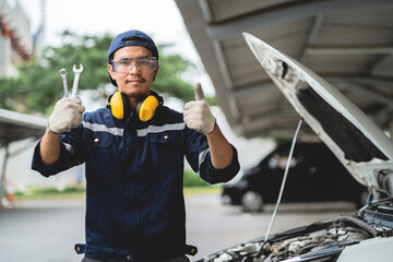 Confident Asian auto mechanic holds a wrench and inspects the maintenance vehicle as per customer's...