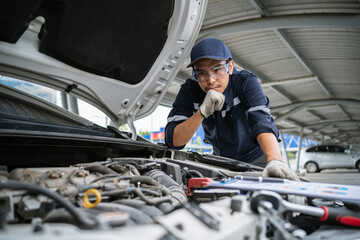 Portrait of an Asian mechanic checking the safety of a car. Maintenance of damaged parts in the garage. Maintenance repairs. Repair service concept.