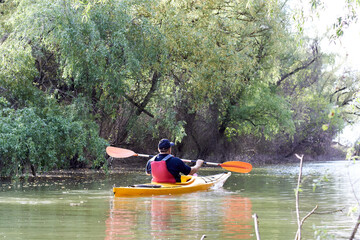 Middle aged man paddle yellow kayak near green trees at spring