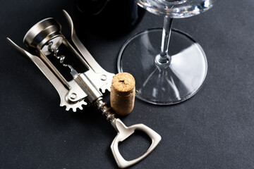 Close-up of a corkscrew opening a bottle of wine. The cork is pierced by the black metal spiral of...