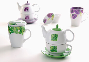 Tea ceramic set with two purple and green tea kettles and cups, and two mugs with infusers, isolated on white