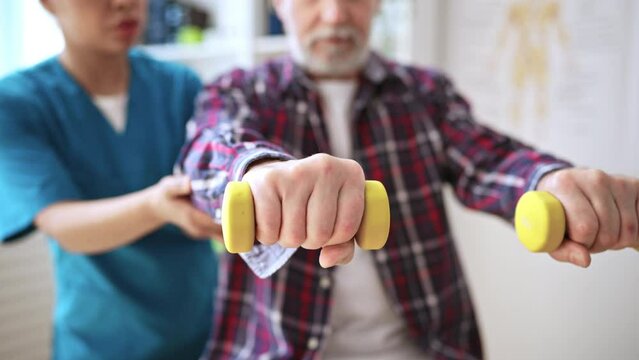 Closeup of doctor helping her senior patient exercise with dumbbells, treatment