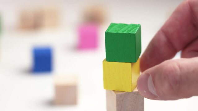 Assembling a toy colored wooden block tower with multicolored cubes. Playing hand sets the green top of the pyramid close-up. Development, education and creativity concept