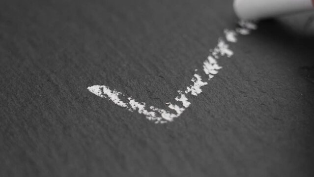 Drawing a check mark with white chalk on a black stone chalkboard. Choice and agreement symbol