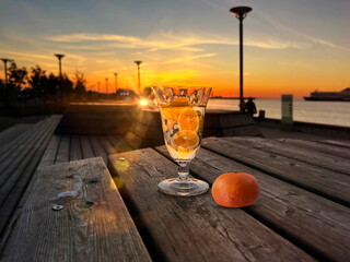 glass of orange water freshness  on wooden table on promenade at sunset in sea summer background 