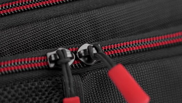 A hand closes the zipper of a black red nylon travel backpack close-up. Safety luggage on trip concept