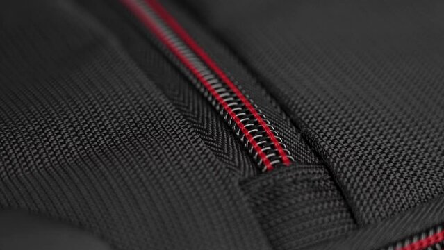 A hand closes the zipper of a black red nylon travel backpack close-up. Safety luggage on trip concept