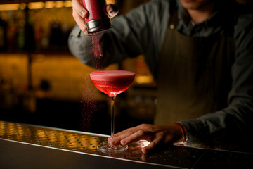 wine glass full of cocktail with tomato juice and hand of bartender pouring red powder on it