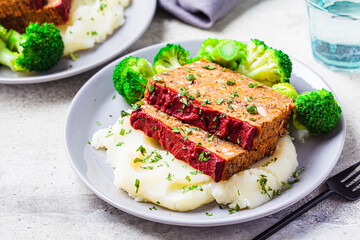 Lentil meatloaf pieces with mashed potatoes and broccoli on gray plate, close-up. Vegan christmas recipe.
