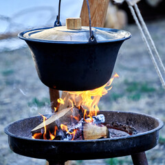 Cast iron pot with primitive lid hangs over open fireplace with burning logs