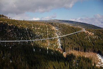 Fototapeta premium Dolni Morava, Czech Republic, 16 April 2022: Path in the clouds, largest suspension bridge in europe, landscape with forest and sky on mountains, Skywalk with snow, mountain lift, restaurant