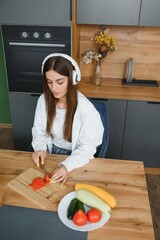Adorable nice charming cheerful pretty beautiful stylish excited girl listening to music, singing in modern light white kitchen, cooking homemade dish with domestic products